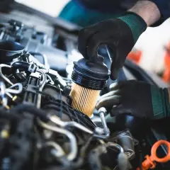 Mechanik w czarnych rękawiczkach dokonuje wymiany filtra paliwa w silniku samochodu.