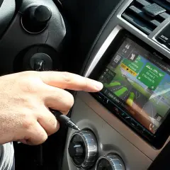Dłoń kierowcy dotyka ekranu nawigacji z mapą, która wygląda jak z systemu radio android auto.