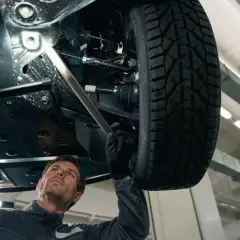 Mechanik bada podwozie samochodu, szukając przyczyny rytmicznego stukania podczas jazdy.
