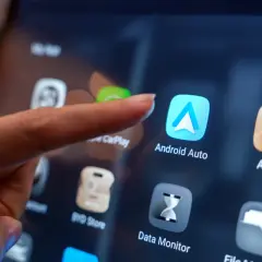 Palec dotyka ikony Android Auto na ekranie, pokazując, jak dodać aplikacje do Android Auto.