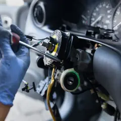 Mechanik w niebieskich rękawiczkach naprawia kolumnę kierownicy. Zastanawiasz się, ile kosztuje przełożenie kierownicy?