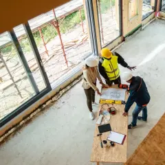 Architekci omawiają plany budowy, analizując wymiana progów cena. Na stole plany, narzędzia i próbki materiałów.