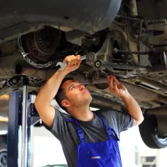 Mechanik w niebieskim kombinezonie dokonuje wymiany tulei wahacza, używając klucza.