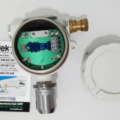 Otwarty detektor gazu z widoczną płytką drukowaną. Obok leży biała pokrywa z napisem "KEEP COVER TIGHT WHEN CIRCUITS ARE LIVE". To może być upg co to jest?