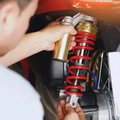 Mechanik dokonuje wymiany amortyzatorów tył w skuterze. Złoty element jest montowany do czerwonej sprężyny.