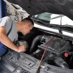 Mechanik pochyla się nad silnikiem, przygotowując się do wymiany świec żarowych.