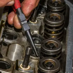 Mechanik używa przyrządu do wymiany uszczelniaczy zaworowych bez zdejmowania głowicy, pracując nad silnikiem.