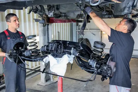Mechanicy pracują nad zarabianiem przewodów hamulcowych przy podniesionym zawieszeniu samochodu.