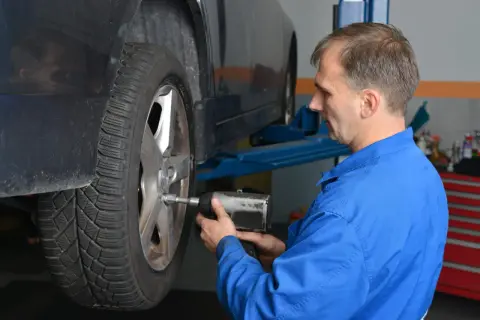 Mechanik w niebieskim kombinezonie dokręca koło kluczem pneumatycznym, pokazując, z jaką siłą dokręcać koła.
