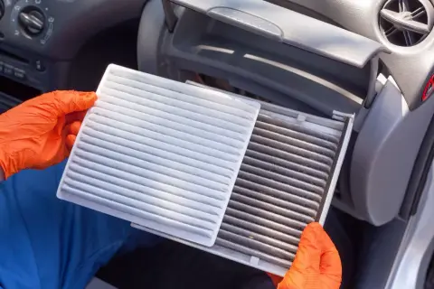 Rękawiczki pomagają w wymianie filtra kabinowego. Nowy, biały filtr obok starego, brudnego.