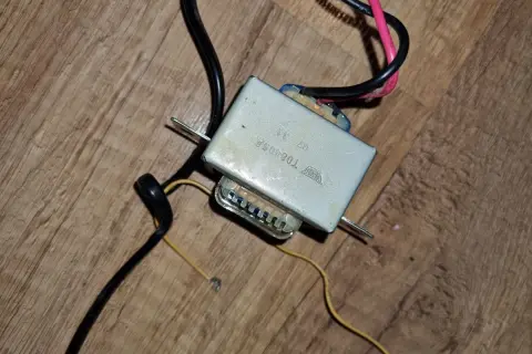 Stary zasilacz do radia samochodowego, z widocznymi przewodami i metalową obudową.