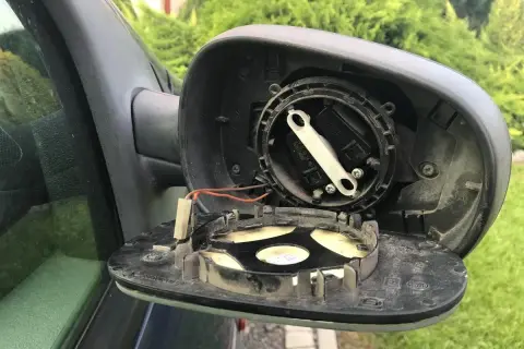 Rozpoczęta wymiana wkładu lusterka. Widoczne mechanizmy regulacji i przewody.