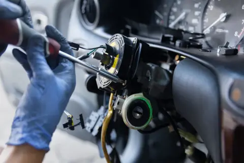 Mechanik w niebieskich rękawiczkach naprawia kolumnę kierownicy. Zastanawiasz się, ile kosztuje przełożenie kierownicy?