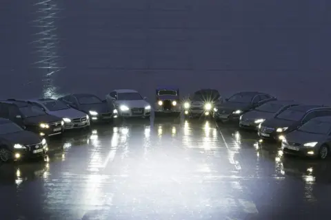 Rząd samochodów z włączonymi światłami, porównanie xenon vs led.