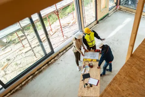 Architekci omawiają plany budowy, analizując wymiana progów cena. Na stole plany, narzędzia i próbki materiałów.