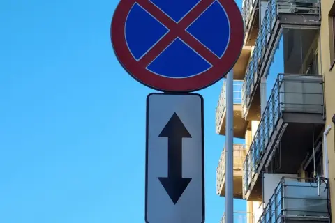 Znak zakaz parkowania ze strzałką w górę i w dół informuje, że postój jest zabroniony po obu stronach drogi.