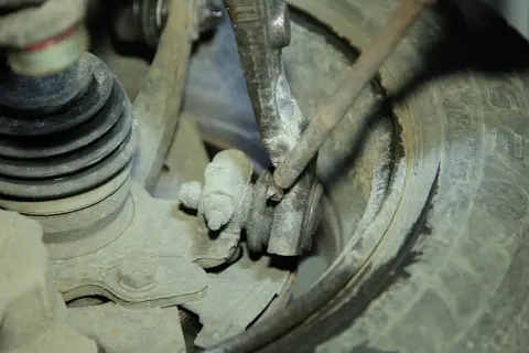 Mechanizm zawieszenia samochodu, podejrzewany o skrzypienie przy skręcaniu. Widoczny przegub kulowy i osłona amortyzatora.
