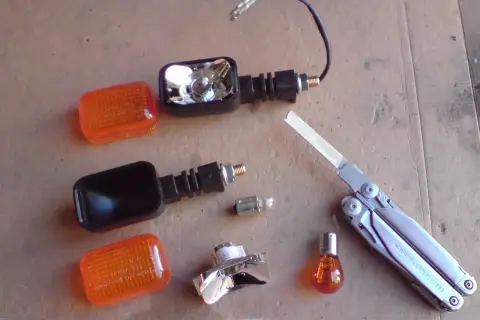 Części do wymiany żarówki kierunkowskazu motocykla: pomarańczowe klosze, obudowy, żarówki, multitool Leatherman Surge.