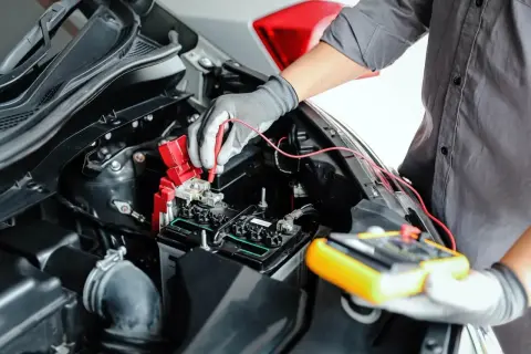 Mechanik w rękawiczkach sprawdza akumulator miernikiem, pokazując, jak sprawdzić alternator miernikiem.
