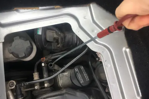 Sprawdzanie poziomu oleju silnikowego: check engine oil level co to znaczy. Dłoń wyciąga miarkę z silnika.