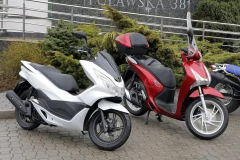 Dwa skutery, biały i czerwony, stoją na mokrym chodniku. Pytanie: co ile wymiana oleju w skuterze 50?