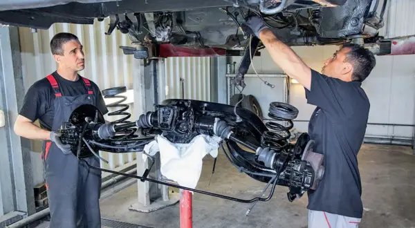 Mechanicy pracują nad zarabianiem przewodów hamulcowych przy podniesionym zawieszeniu samochodu.