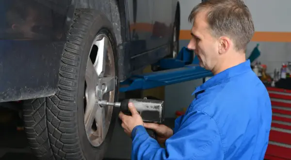 Mechanik w niebieskim kombinezonie dokręca koło kluczem pneumatycznym, pokazując, z jaką siłą dokręcać koła.