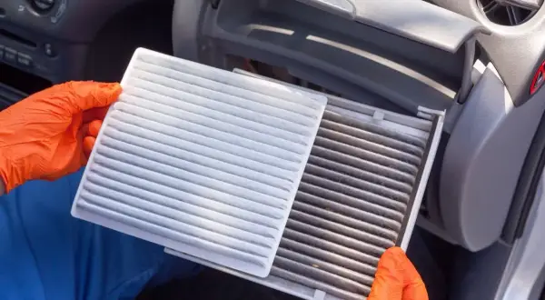 Rękawiczki pomagają w wymianie filtra kabinowego. Nowy, biały filtr obok starego, brudnego.