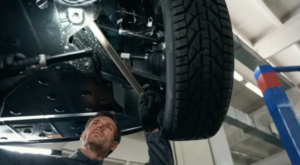 Mechanik bada podwozie samochodu, szukając przyczyny rytmicznego stukania podczas jazdy.