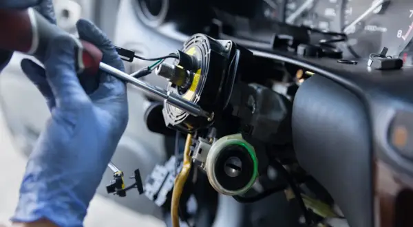 Mechanik w niebieskich rękawiczkach naprawia kolumnę kierownicy. Zastanawiasz się, ile kosztuje przełożenie kierownicy?
