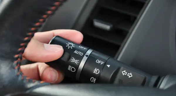 Dłoń manipuluje przełącznikiem świateł w samochodzie, ustawiając go na pozycję "AUTO".
