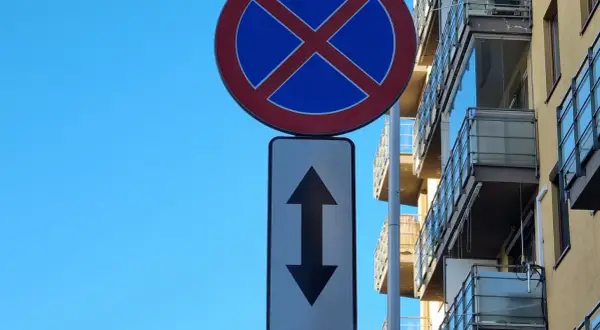 Znak zakaz parkowania ze strzałką w górę i w dół informuje, że postój jest zabroniony po obu stronach drogi.