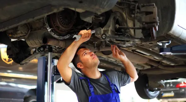 Mechanik w niebieskim kombinezonie dokonuje wymiany tulei wahacza, używając klucza.