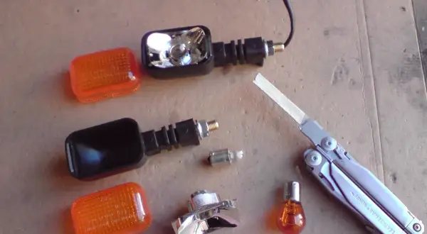 Części do wymiany żarówki kierunkowskazu motocykla: pomarańczowe klosze, obudowy, żarówki, multitool Leatherman Surge.
