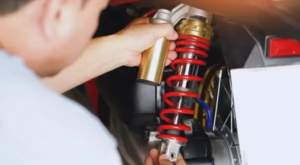 Mechanik dokonuje wymiany amortyzatorów tył w skuterze. Złoty element jest montowany do czerwonej sprężyny.