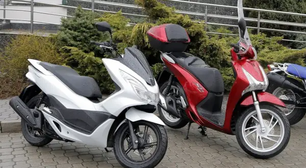Dwa skutery, biały i czerwony, stoją na mokrym chodniku. Pytanie: co ile wymiana oleju w skuterze 50?