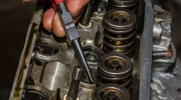 Mechanik używa przyrządu do wymiany uszczelniaczy zaworowych bez zdejmowania głowicy, pracując nad silnikiem.