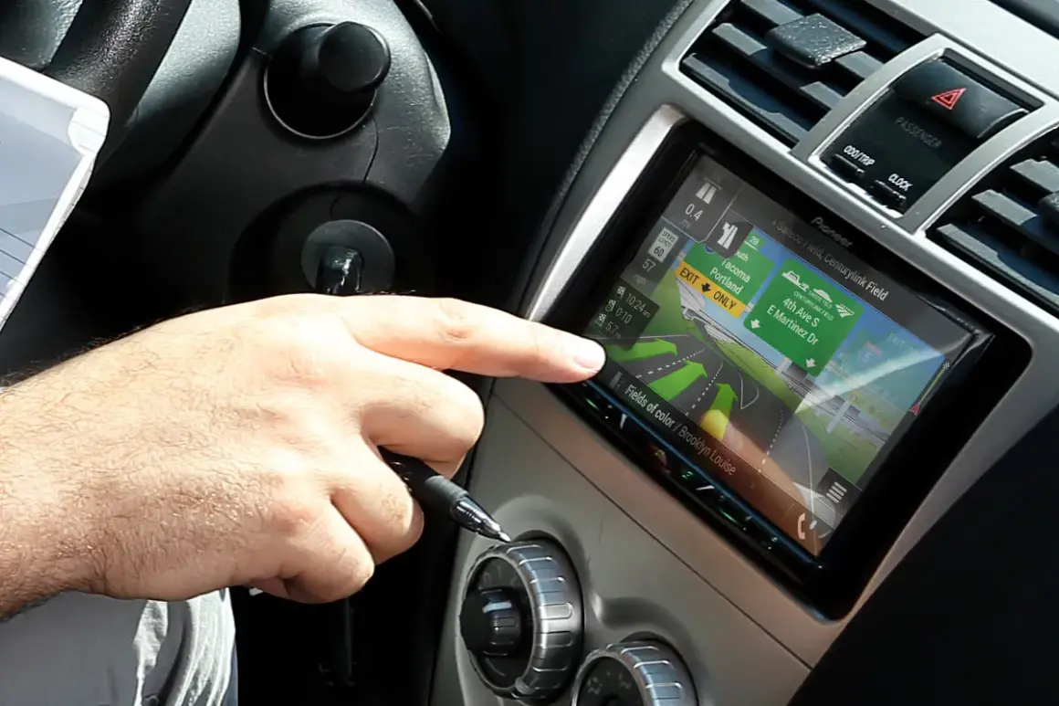 Dłoń kierowcy dotyka ekranu nawigacji z mapą, która wygląda jak z systemu radio android auto.