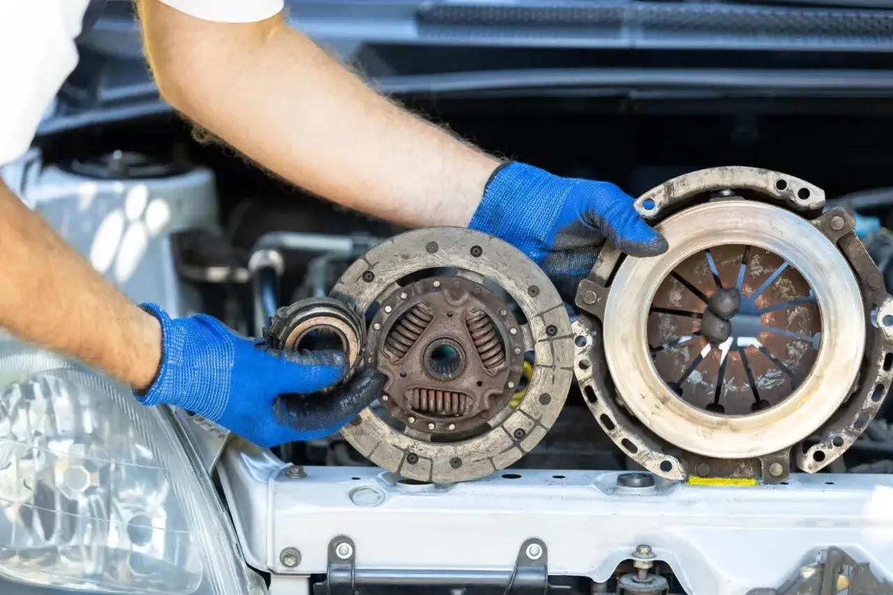 Mechanik w niebieskich rękawicach pokazuje zużyte części: tarczę i docisk sprzęgła. Wymiana ślizgającego się sprzęgła jest kluczowa.