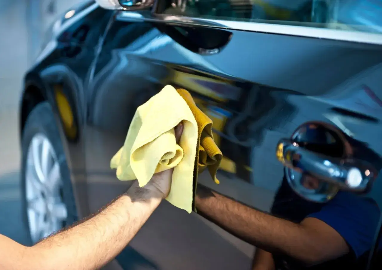 Ręka poleruje czarne auto żółtą mikrofibrą, nadając mu połysk. Zastanawiasz się, jaki wosk do auta wybrać?
