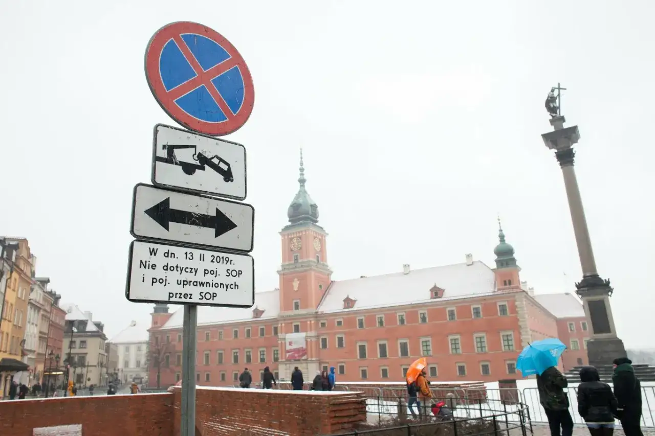 Znak zakaz parkowania ze strzałką w obie strony. W tle Zamek Królewski w Warszawie.