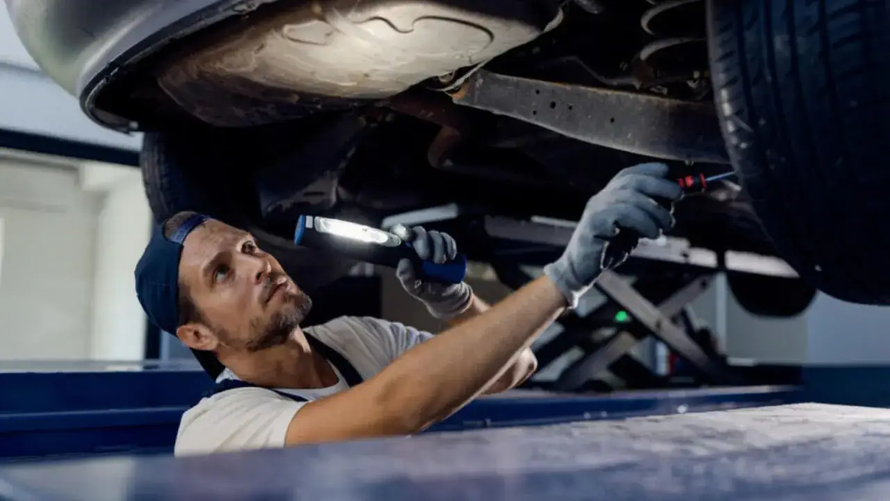Mechanik z latarką bada podwozie auta, szukając przyczyny rytmicznego stukania podczas jazdy.
