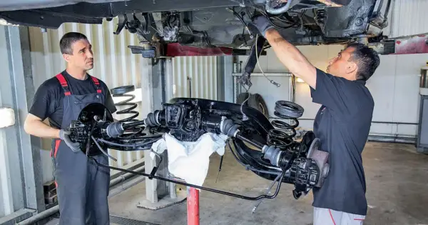 Mechanicy pracują nad zarabianiem przewodów hamulcowych przy podniesionym zawieszeniu samochodu.