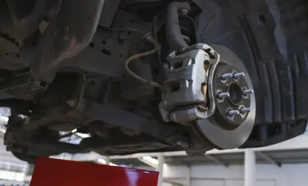 Widok od dołu na zawieszenie samochodu z widocznym hamulcem tarczowym. Pojedynczy stuk przy skręcaniu może oznaczać problem z tym elementem.