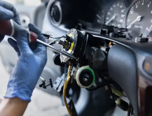 Mechanik w niebieskich rękawiczkach naprawia kolumnę kierownicy. Zastanawiasz się, ile kosztuje przełożenie kierownicy?