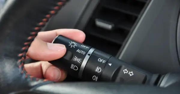 Dłoń manipuluje przełącznikiem świateł w samochodzie, ustawiając go na pozycję "AUTO".