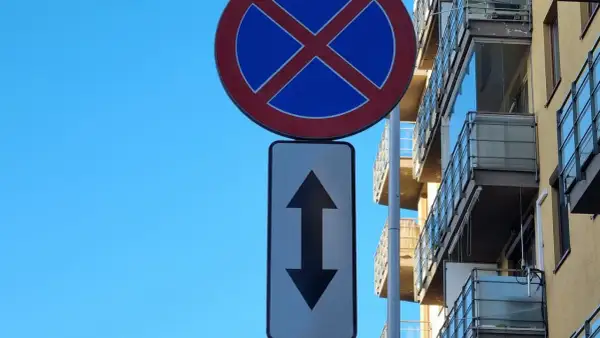 Znak zakaz parkowania ze strzałką w górę i w dół informuje, że postój jest zabroniony po obu stronach drogi.