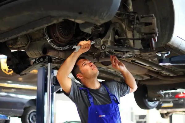 Mechanik w niebieskim kombinezonie dokonuje wymiany tulei wahacza, używając klucza.