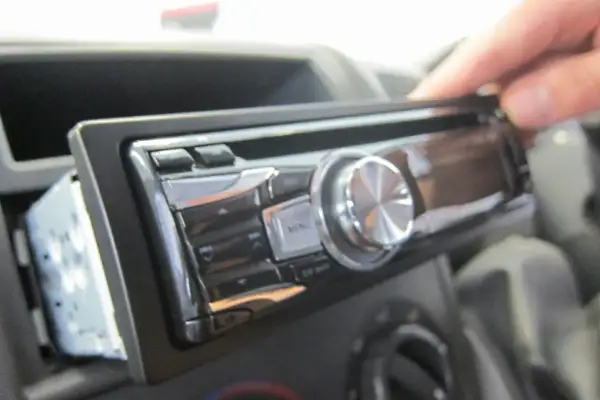 Dłoń wyjmuje radio samochodowe. Może to być pierwszy krok, jak znaleźć kod do radia, jeśli go zapomniałeś.
