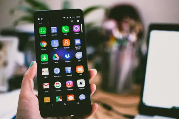 Dłoń trzyma smartfon z ikonami aplikacji, pokazując jak otworzyć schowek. Widoczne m.in. Gmail, Google, Instagram.